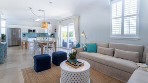 Una sala de estar moderna con un sofá, otomanas, una mesa de centro y un comedor con sillas y una mesa.