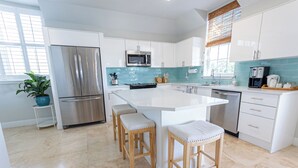 Una cocina moderna con armarios blancos, electrodomésticos de acero inoxidable, una isla grande con taburetes y un salpicadero verde azulado.