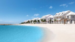 Un hotel frente a la playa con edificios de varios pisos, fachadas blancas y una playa de arena.