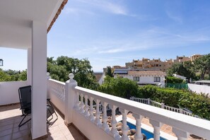 A balcony with a white balustrade, a black chair, and a view of buildings and greenery. - Villa Blue Skies - Calahonda (Sitio de Calahonda)