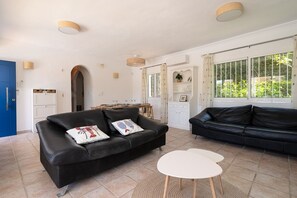 A living room with two black sofas, a white coffee table, and a kitchen area with a dining table. - Villa Blue Skies - Calahonda (Sitio de Calahonda)