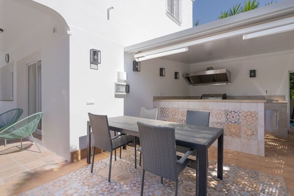 An outdoor kitchen area with a dining table and chairs, a built-in grill, and a tiled backsplash. - Villa Blue Skies - Calahonda (Sitio de Calahonda)