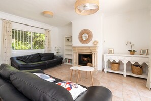 A living room with a fireplace, a sofa, a coffee table, and a white console table with baskets. - Villa Blue Skies - Calahonda (Sitio de Calahonda)