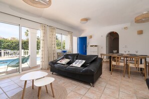 Una sala de estar con un sofá de cuero negro, una mesa de comedor con sillas, vista a la piscina y una zona de cocina.