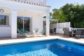 Una piscina con un diseño geométrico de azulejos, rodeada de mobiliario exterior con sillas y mesas.