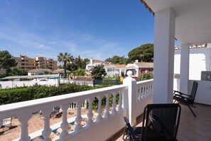 A balcony with a white balustrade, two black chairs, and a view of a residential area with buildings and a pool. - Villa Blue Skies - Calahonda (Sitio de Calahonda)
