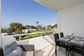 Een balkon met een eettafel, stoelen en uitzicht op zee en groen.