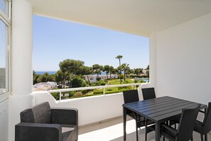 A balcony with a table and chairs, overlooking a green landscape and a body of water.