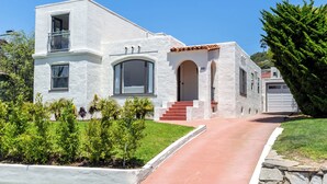 Une maison blanche aux murs recouverts d’enduit, avec un toit de tuiles rouges, un balcon et un chemin de pierre menant à l’entrée.