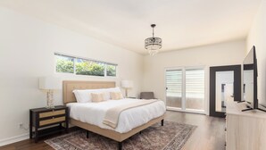 Une chambre à coucher comprenant un lit, des tables de chevet, un lustre, une grande fenêtre et une porte-fenêtre coulissante.