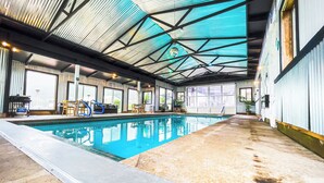 Une piscine intérieure dotée d’un toit en verre, entourée d’espaces de détente et de grandes fenêtres.