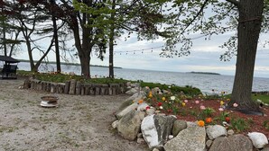 A lakeside outdoor seating area with a fire pit, stone walls, and flower beds. - Goffatt Island-your private island 1+1 Bedroom Cabin 201 (Goffatt Island)