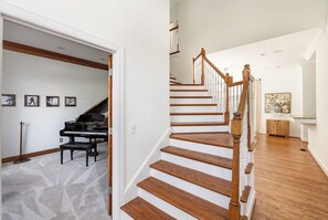 Staircase leads to an upper level, featuring a grand piano in a spacious music room.