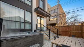 A hot tub with a wooden deck, a table with chairs, and a wooden fence in a backyard. - La More | Hot Tub | Kensington | Luxury | Office (Calgary)