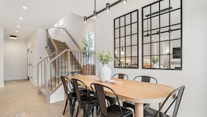 A modern dining area with a wooden table, black chairs, and a large window with a grid pattern. - La More | Hot Tub | Kensington | Luxury | Office (Calgary)