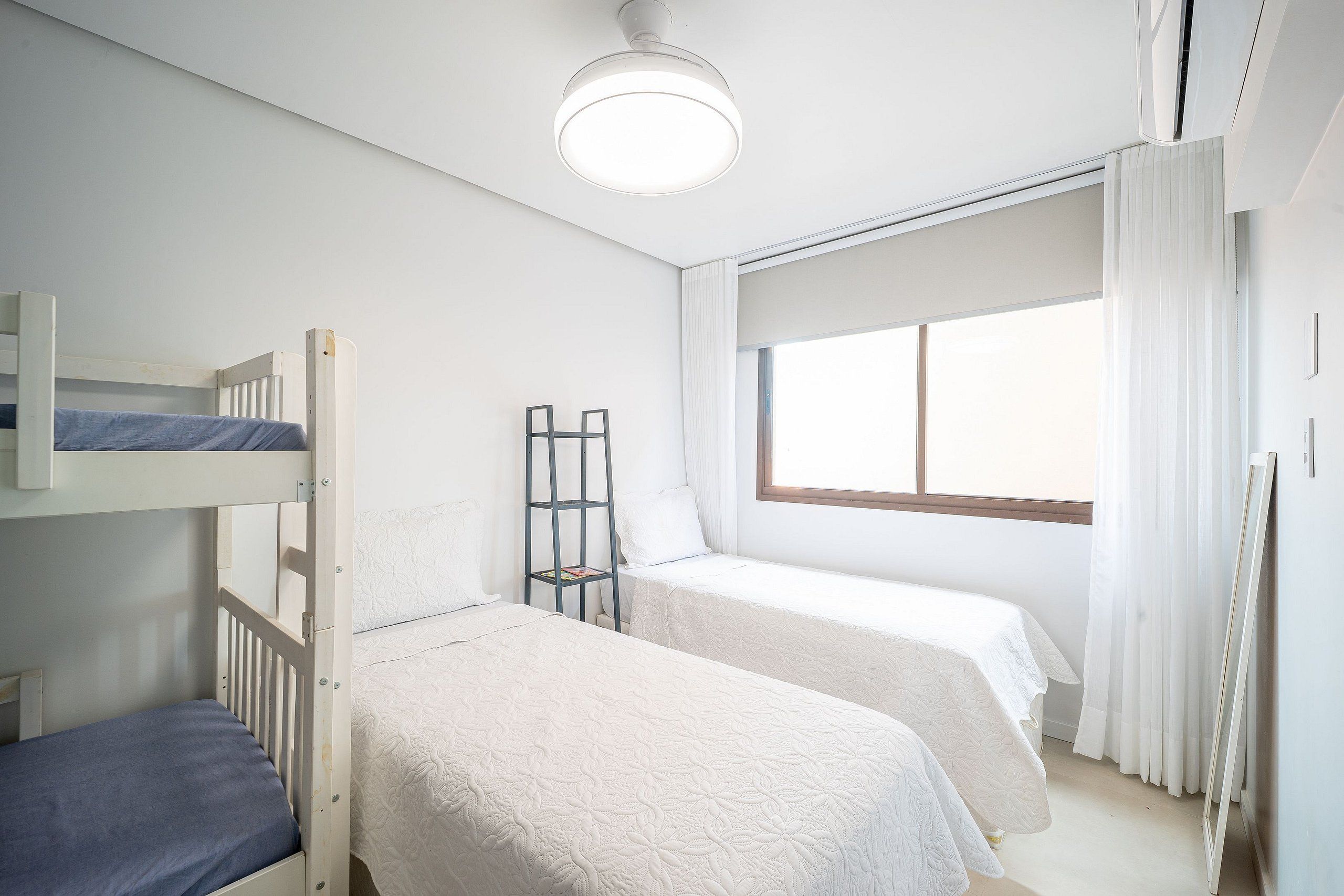 A bedroom with bunk beds, a window with curtains, and a ceiling light.