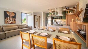 A modern living room with a sofa, dining table set for four, and a kitchen in the background.