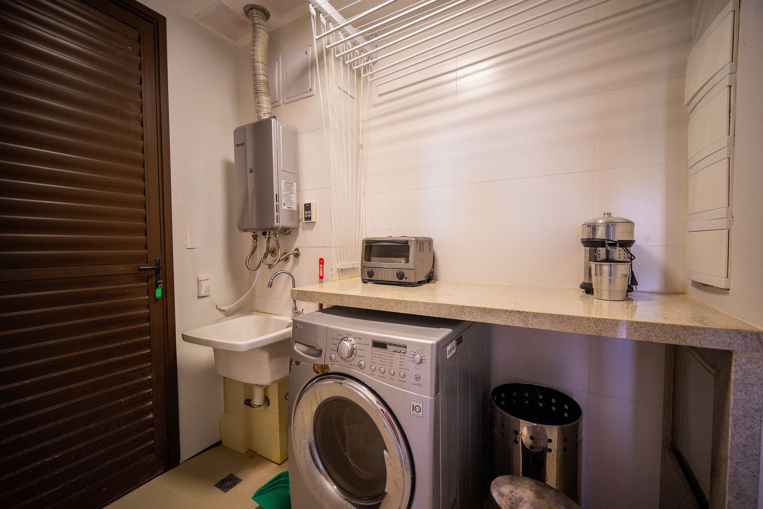 A compact laundry area with a washing machine, a sink, and a small countertop with a kettle and a microwave.