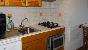 A kitchen with wooden cabinets, a gas stove, a sink, and a built-in oven. - Central Studio for 2 with Balcony, Wi-Fi, Linens & Towels Included (Les Gets)