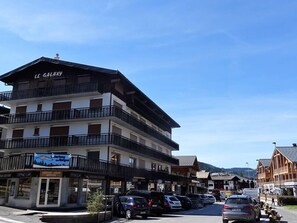 A multi-story hotel with balconies, a ski resort sign, and parked cars on the street. - Central Studio for 2 with Balcony, Wi-Fi, Linens & Towels Included (Les Gets)