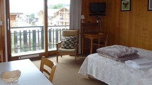 A hotel room with a balcony, a bed, a desk, a chair, and a television. - Central Studio for 2 with Balcony, Wi-Fi, Linens & Towels Included (Les Gets)