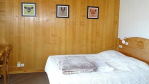 A wooden-paneled room with a bed, a chair, and three framed pictures on the wall. - Central Studio for 2 with Balcony, Wi-Fi, Linens & Towels Included (Les Gets)