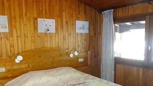 A wooden cabin room with a bed, a headboard with a floral design, and three framed pictures on the wall. - Spacious 1-Bed Apt in Central Les Gets - 4 Guests, Wi-Fi, Linens Provided (Les Gets)