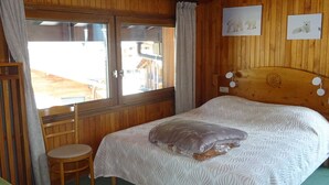 Ein Zimmer mit Holzwänden, einem Bett, einem kleinen Tisch und einem Fenster mit Vorhängen.