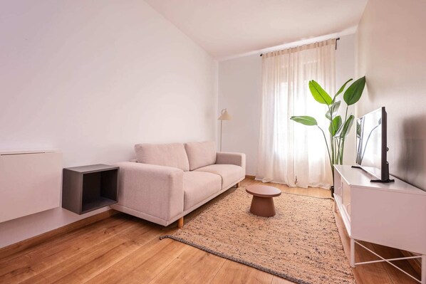 A modern living room with a sofa, a small round table, a TV, and a plant.