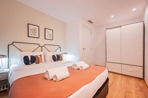 A neatly arranged bedroom with a bed, bedside tables, a wardrobe, and two framed botanical prints on the wall.