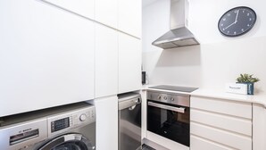 Eine kleine Küche mit einer Bosch Waschmaschine, einem Backofen und einer Uhr an der Wand.