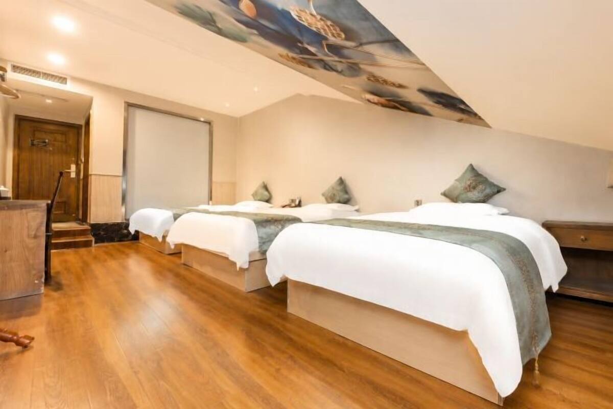 A hotel room with three beds, wooden flooring, and a large painting on the ceiling.