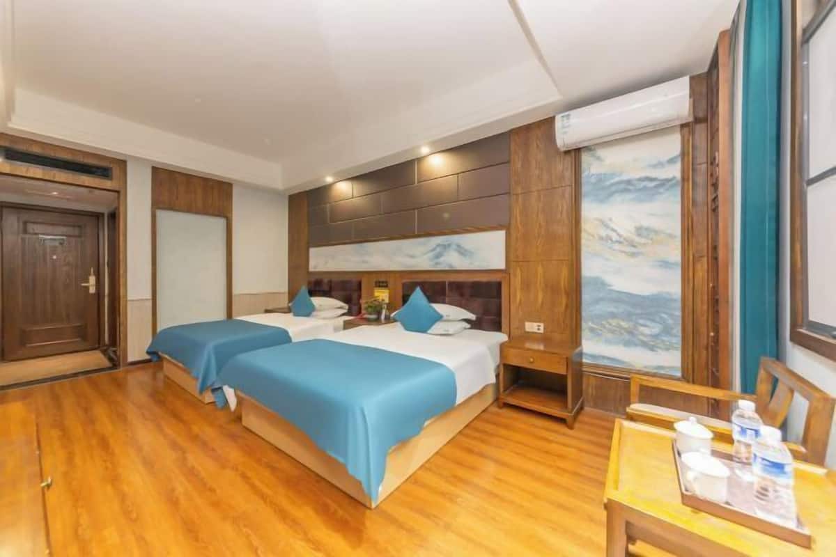 Ein Hotelzimmer mit zwei Betten, Holzboden, einem Bild an der Wand und einem kleinen Tisch mit Tablett.