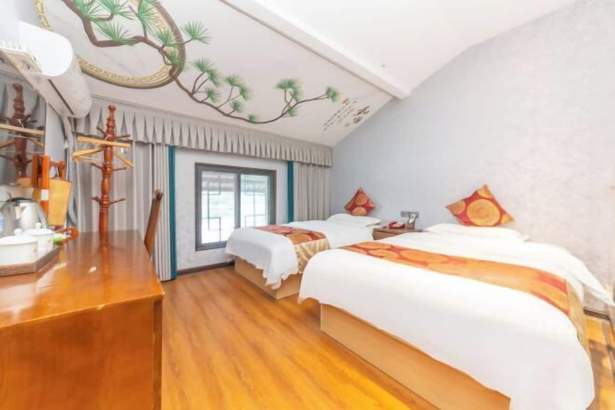A hotel room with two beds, a wooden desk, a window, and a decorative ceiling.