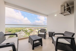 Enjoy the serene view of the surrounding landscape from this balcony, featuring wicker furniture and a distant cityscape.