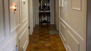 A hallway with a checkered wooden floor, white walls with paneling, a mirror on a table, and a light fixture on the wall.