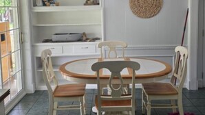 A dining area with a round table and four chairs, a chandelier, a white wall with shelves, and a woven wall hanging.