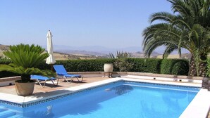 A swimming pool with blue tiles, a white umbrella, and blue lounge chairs.