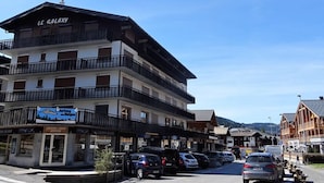 Un hôtel à plusieurs étages doté de balcons, une enseigne indiquant la présence d’une station de ski, et des voitures garées le long de la rue.