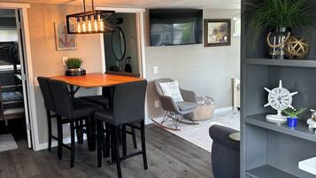Una sala moderna con comedor, una estantería gris y un televisor montado en la pared.