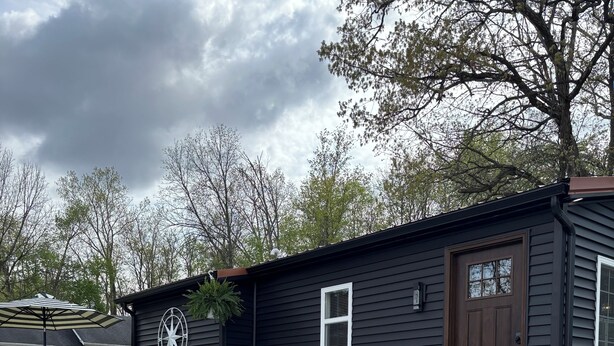 A black house with a patio area featuring outdoor furniture and a grill.
