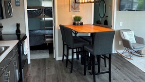 A compact kitchen with modern appliances, a dining area with a wooden table and chairs, and a cozy seating area with a rocking chair.