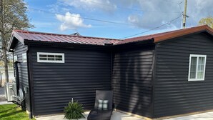 A black single-story house with a red roof, a covered patio, and a small garden area.