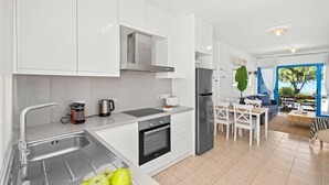 Eine moderne Küche mit weißen Schränken, einer Edelstahlspüle, einem Einbauofen und einem Kühlschrank.