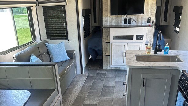 A compact RV interior with a kitchenette, a seating area, and a small bathroom.