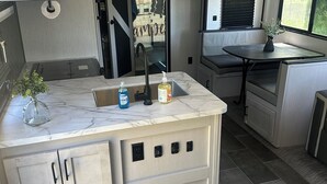 A compact kitchen with a marble countertop, a sink, and a window with a view of trees.