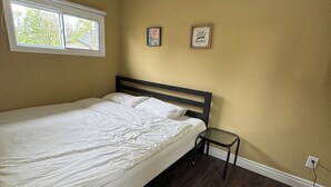 Une chambre à coucher comprenant un lit, une petite table, une fenêtre et deux éléments décoratifs fixés au mur.