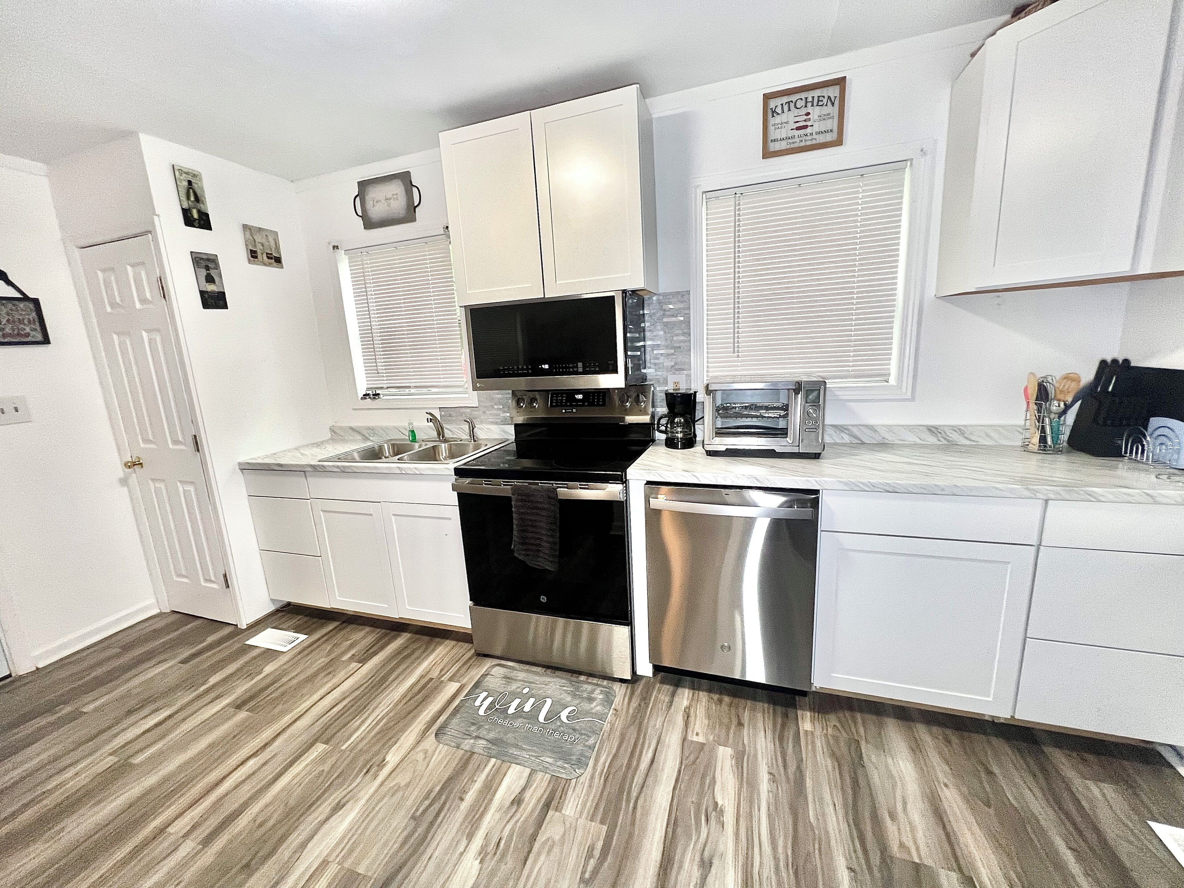 A modern kitchen with white cabinets, stainless steel appliances, and a wooden floor.