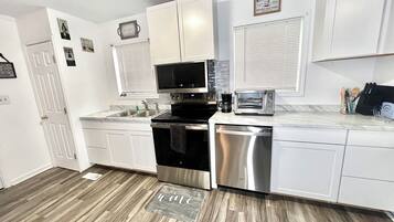 A modern kitchen with white cabinets, stainless steel appliances, and a wooden floor.