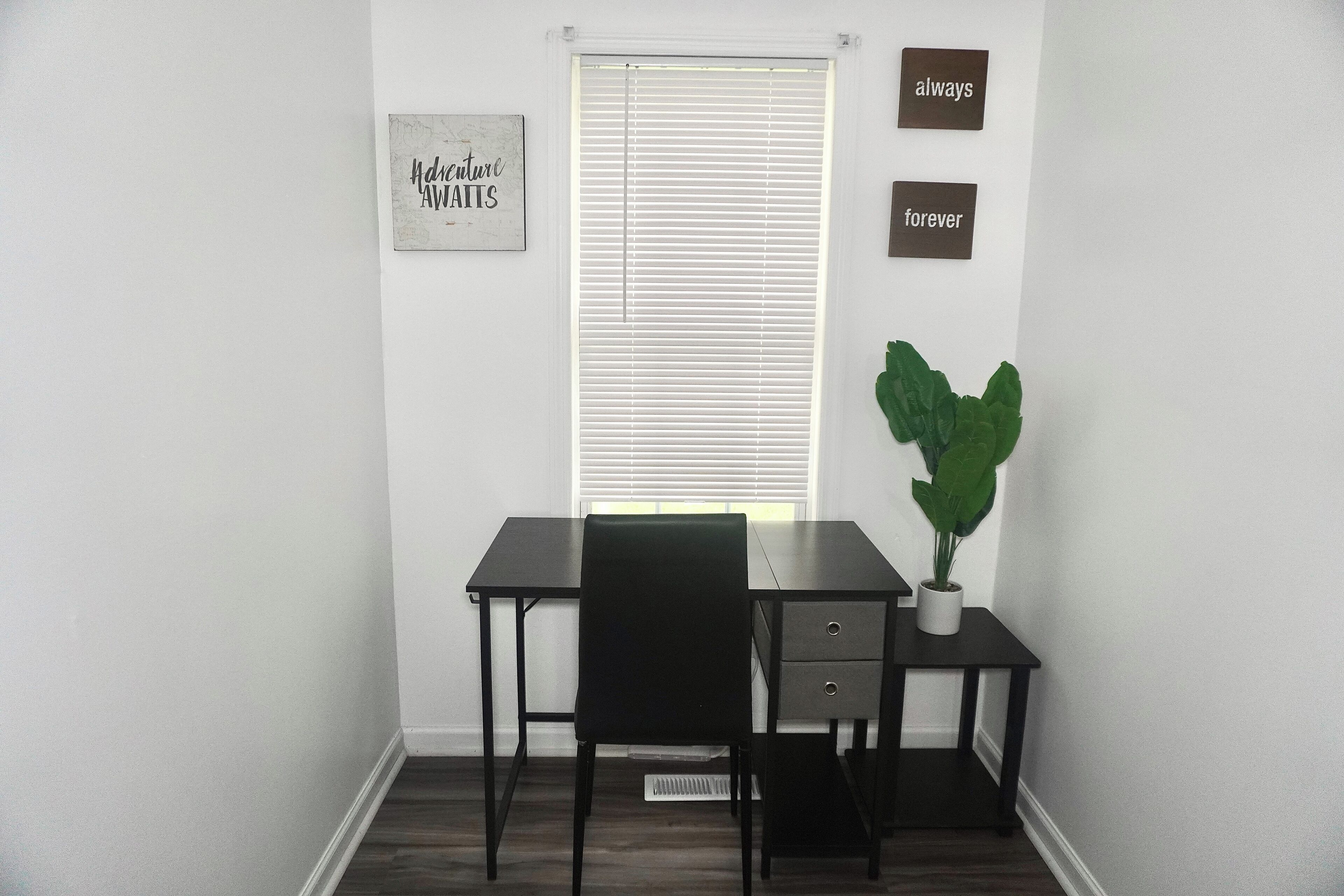 A small, dark wooden desk with two drawers, a black chair, and a potted plant.
